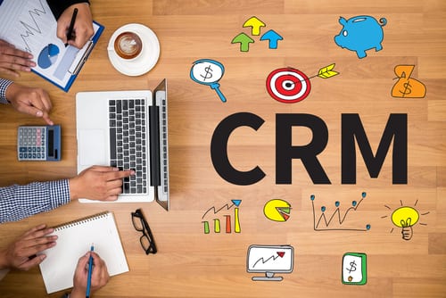 image of a laptop and papers on a table, with CRM written on the table with different diagrams and graphs to represent Customer experience with CRM